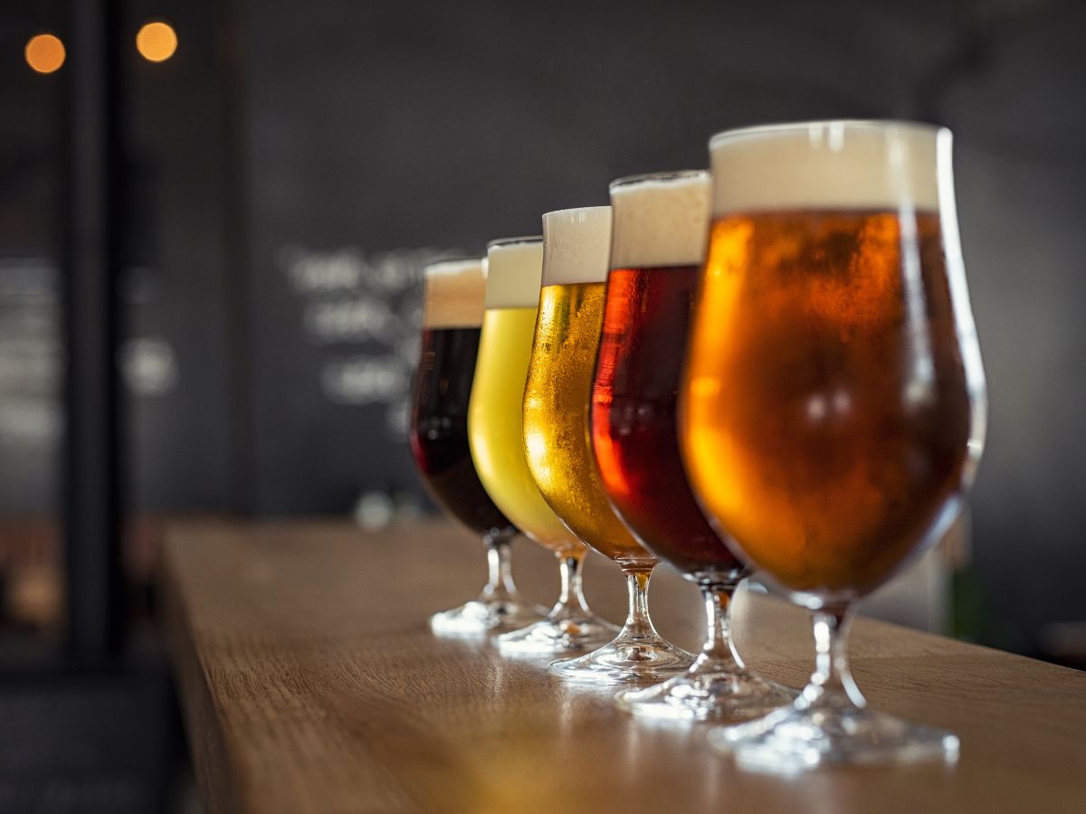 A flight of beers in glasses on a wooden bar.