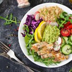 Quinoa bowl with arugula, grilled chicken, vegetables, and guacamole