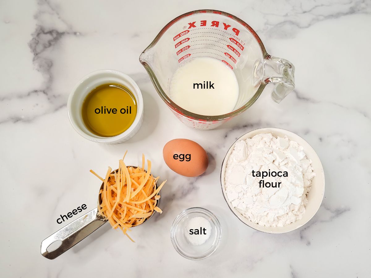 The ingredients needed to make Brazilian cheese bread include olive oil, mik, tapioca flour, and cheese.
