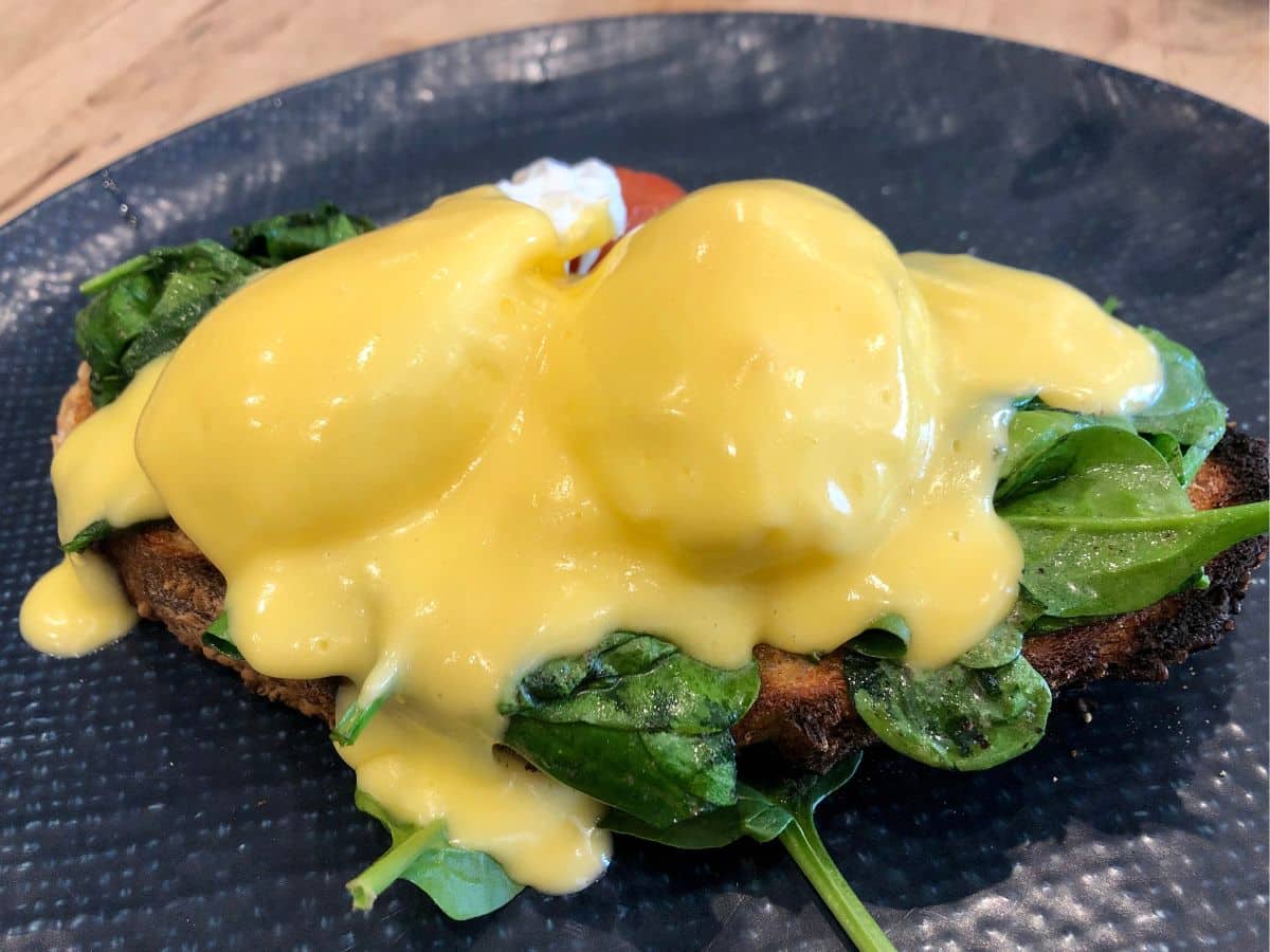 A plate of Benedict-style eggs florentine smothered in hollandaise sauce.