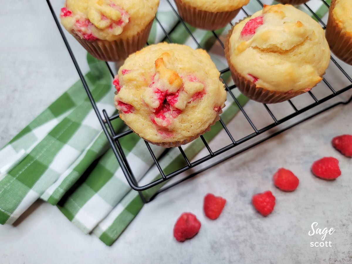 Raspberry muffins on a cooling rack with fresh raspberries.