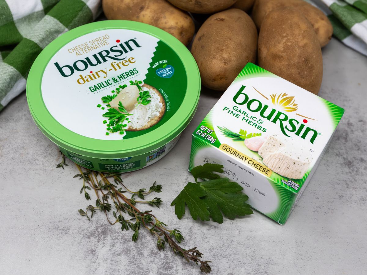 Regular and vegan Boursin cheese on a grey counter with potatoes and herbs