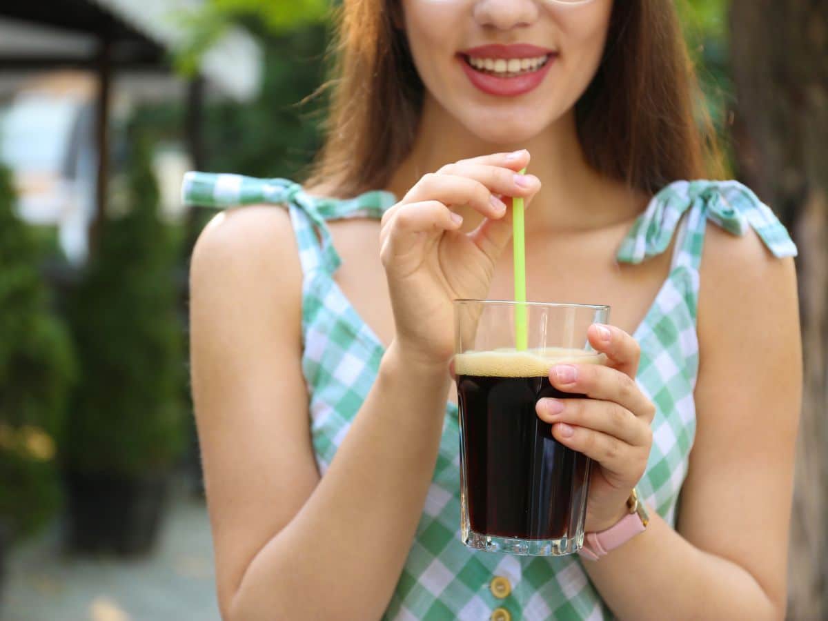 Woman in a checked dress preparing to sip cold brew coffee from a yellow straw