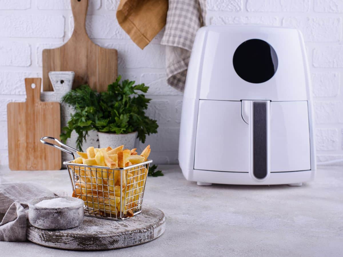 A white air fryer on a kitchen cabinet with a basket of French fries in the foreground