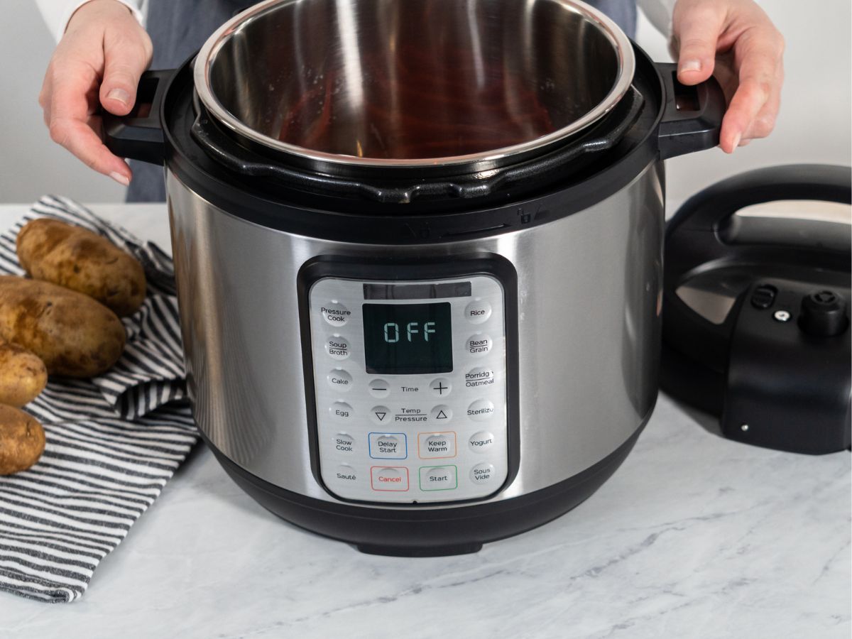A woman holding an Instant Pot with a pile of potatoes nearby