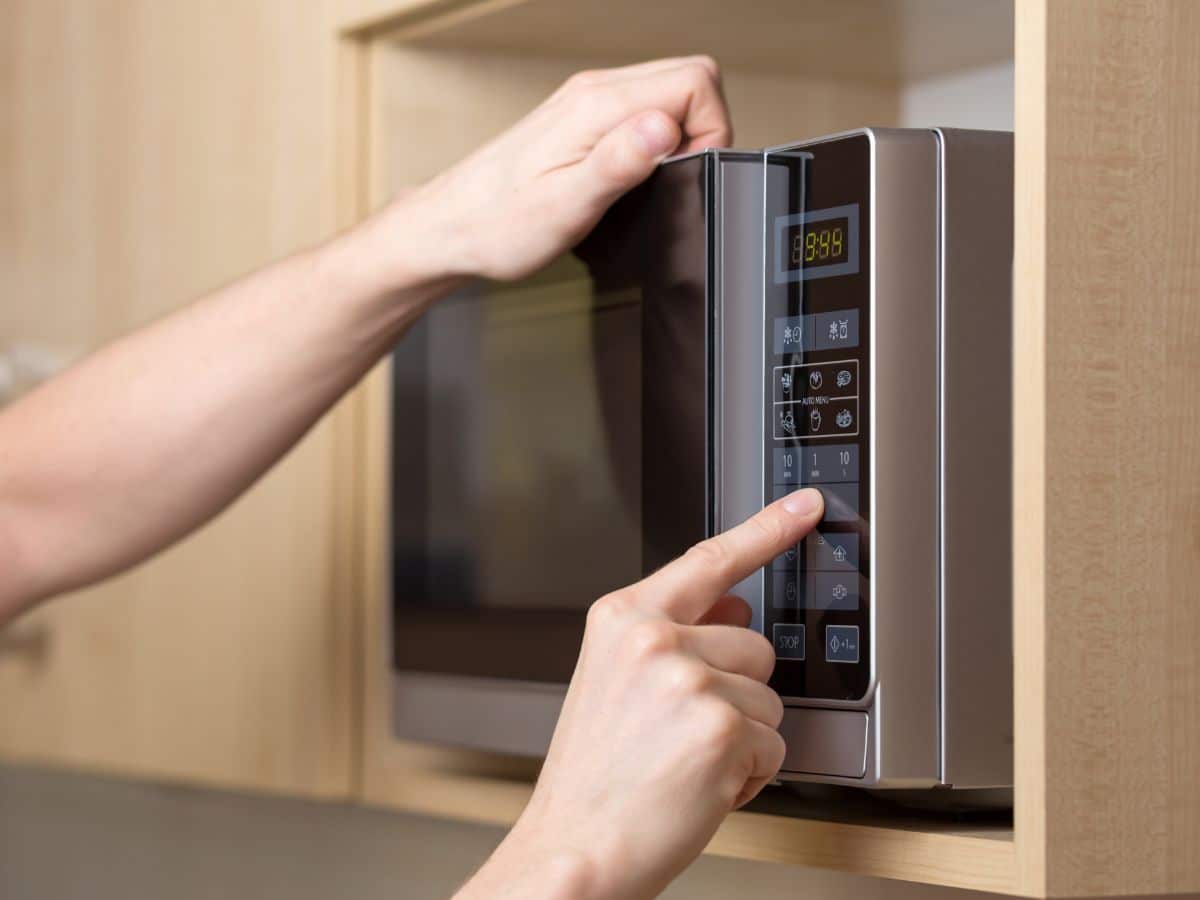 A person pressing the buttons on a microwave.