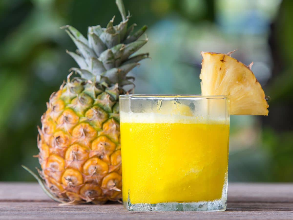 A glass of pineapple juice and a fresh pineapple