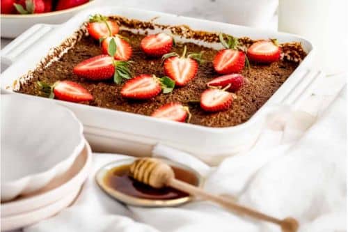 A white baking dish with a quinoa breakfast casserole topped with strawberries and honey.