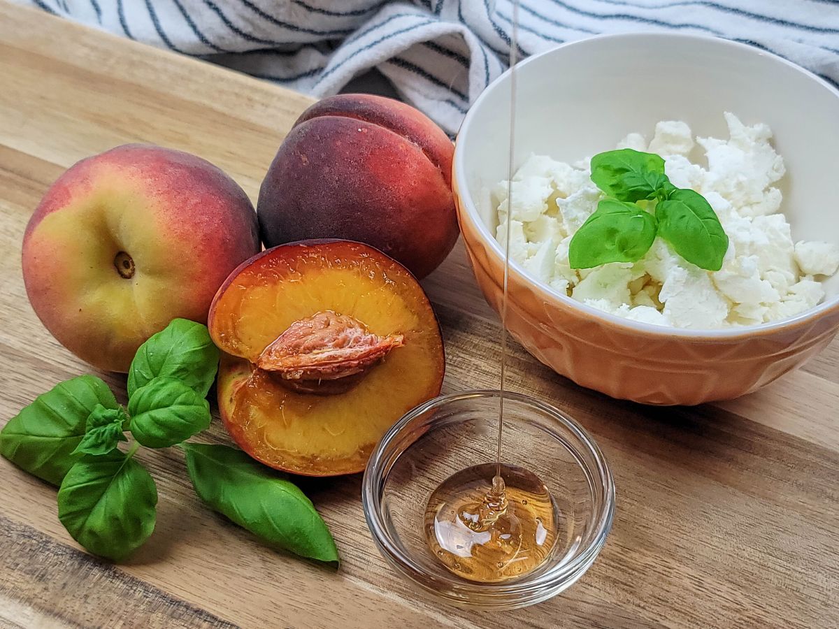 The ingredients needed to make stuffed peaches: fresh peaches, goat cheese, basil, and honey.
