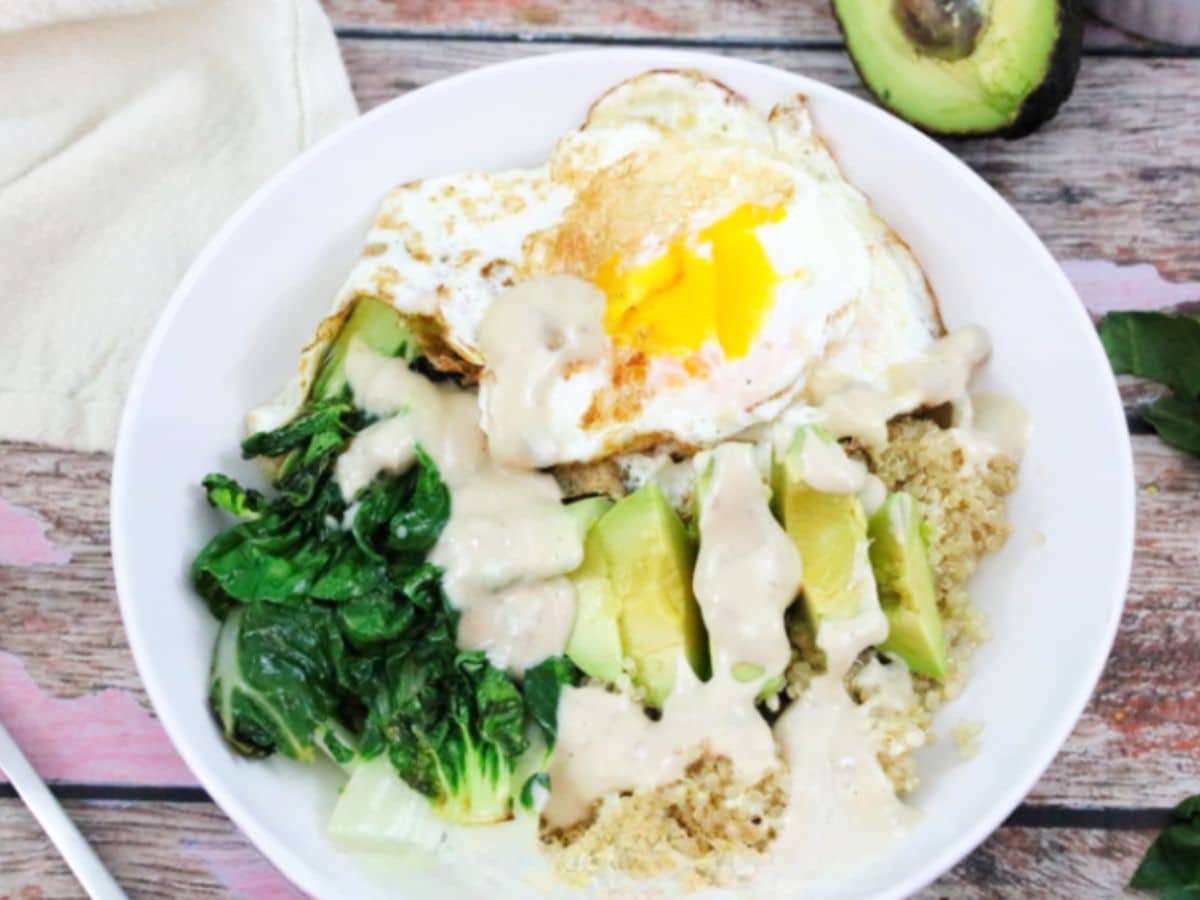 A quinoa bowl with a fried egg, greens, and avocado.