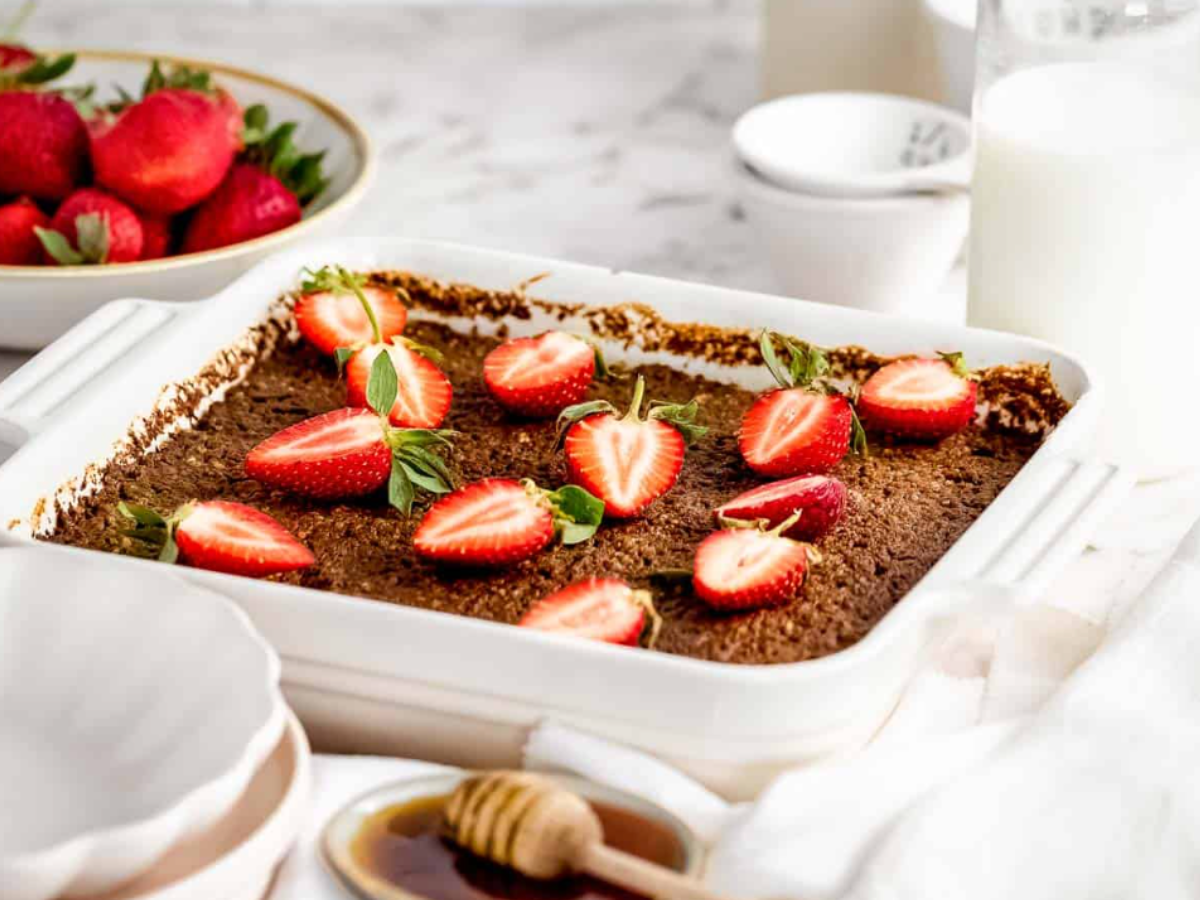 A white casserole dish of baked quinoa topped with sliced strawberries.