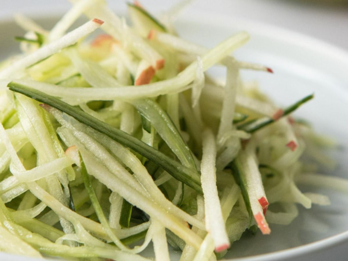 A white plate piled high with apple cucumber salad.