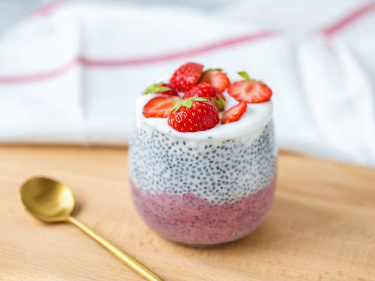 Chia pudding showcasing the benefits of chia seeds with strawberries and cream on a wooden cutting board.