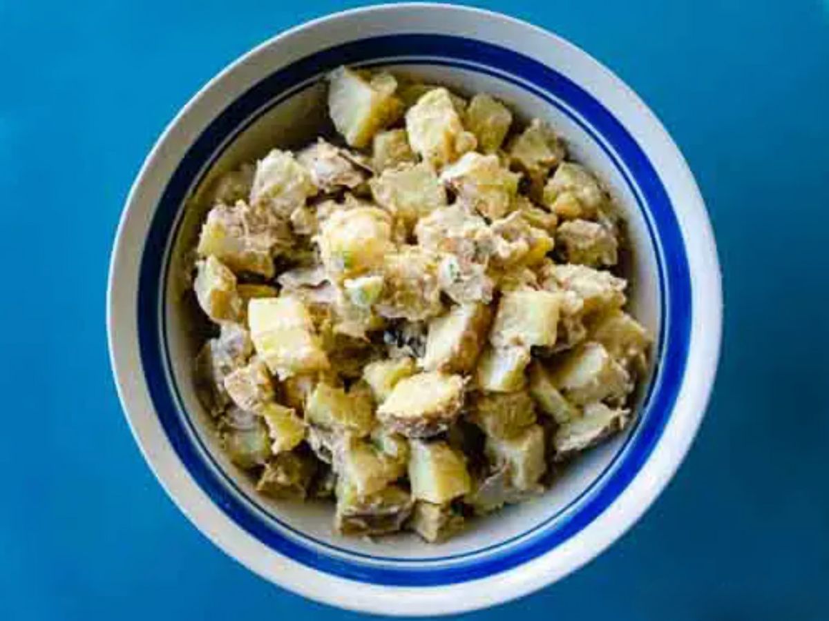 A bowl of creamy potato salad on a blue background.