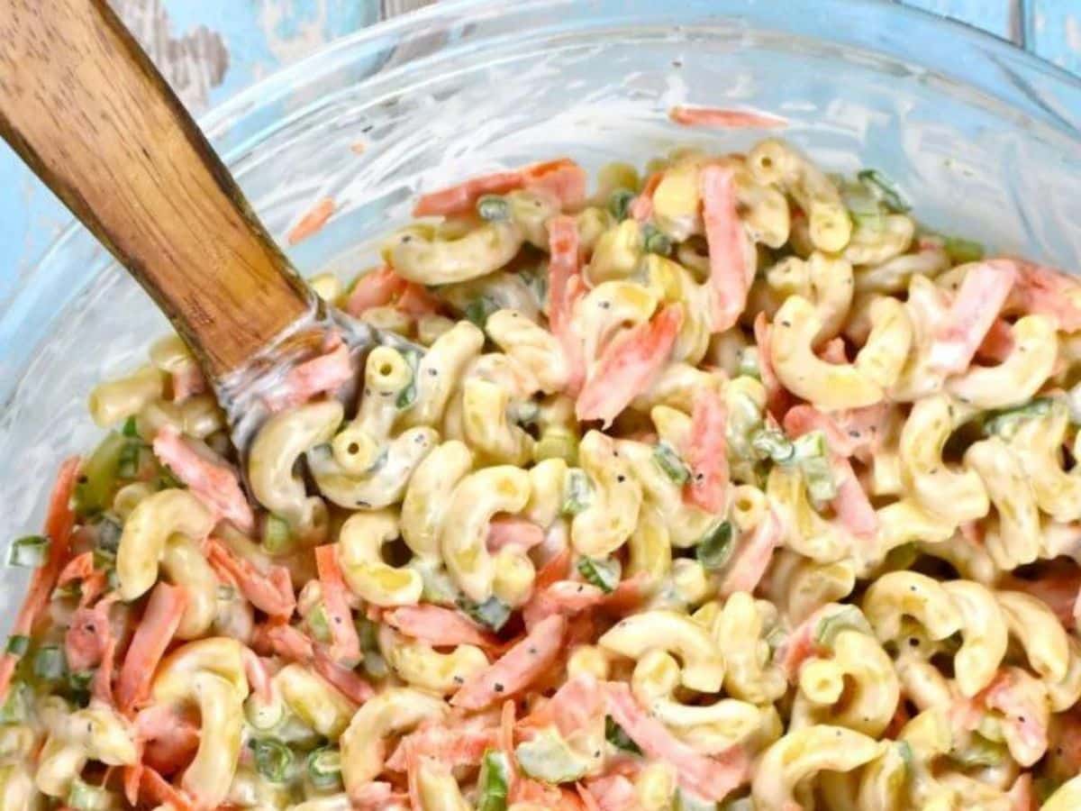 A glass bowl of Hawaiian-style macaroni salad ready to serve with a wooden spoon.