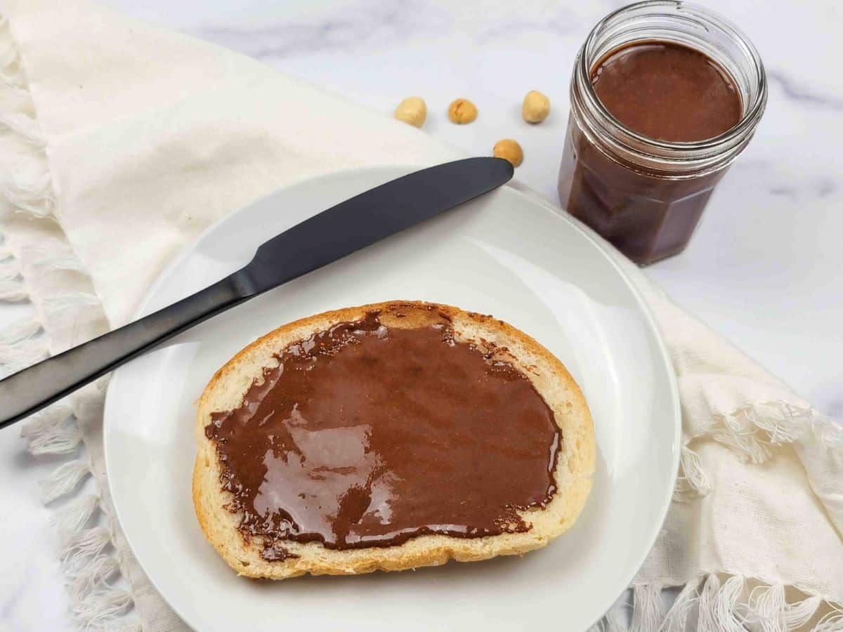 Jar of homemade dairy-free Nutella jar next to a plate with toast and a knife.