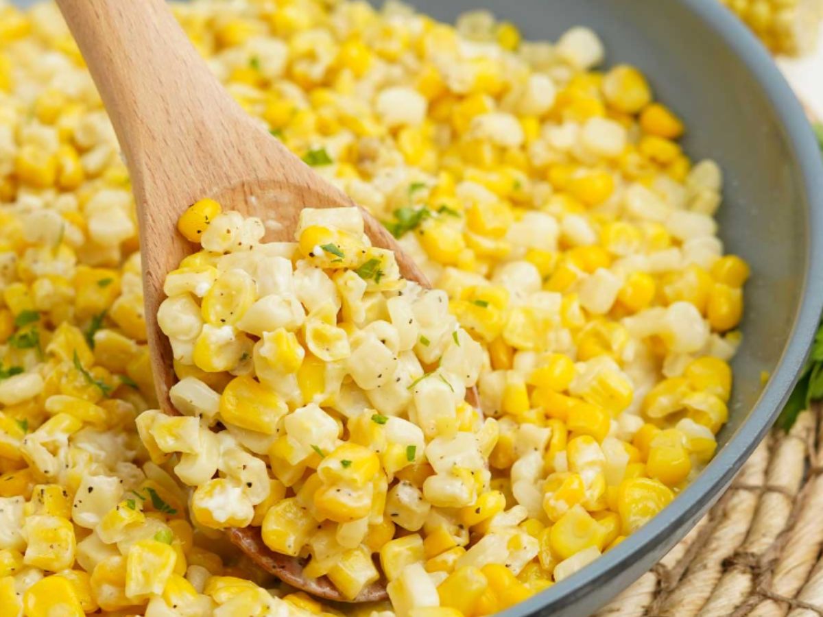A wooden spoon stirring a skillet of honey corn.