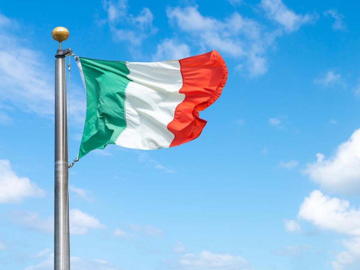The italian flag flies in the wind against a blue sky.