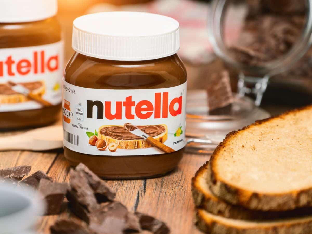 A jar of Nutella and bread on a wooden table.