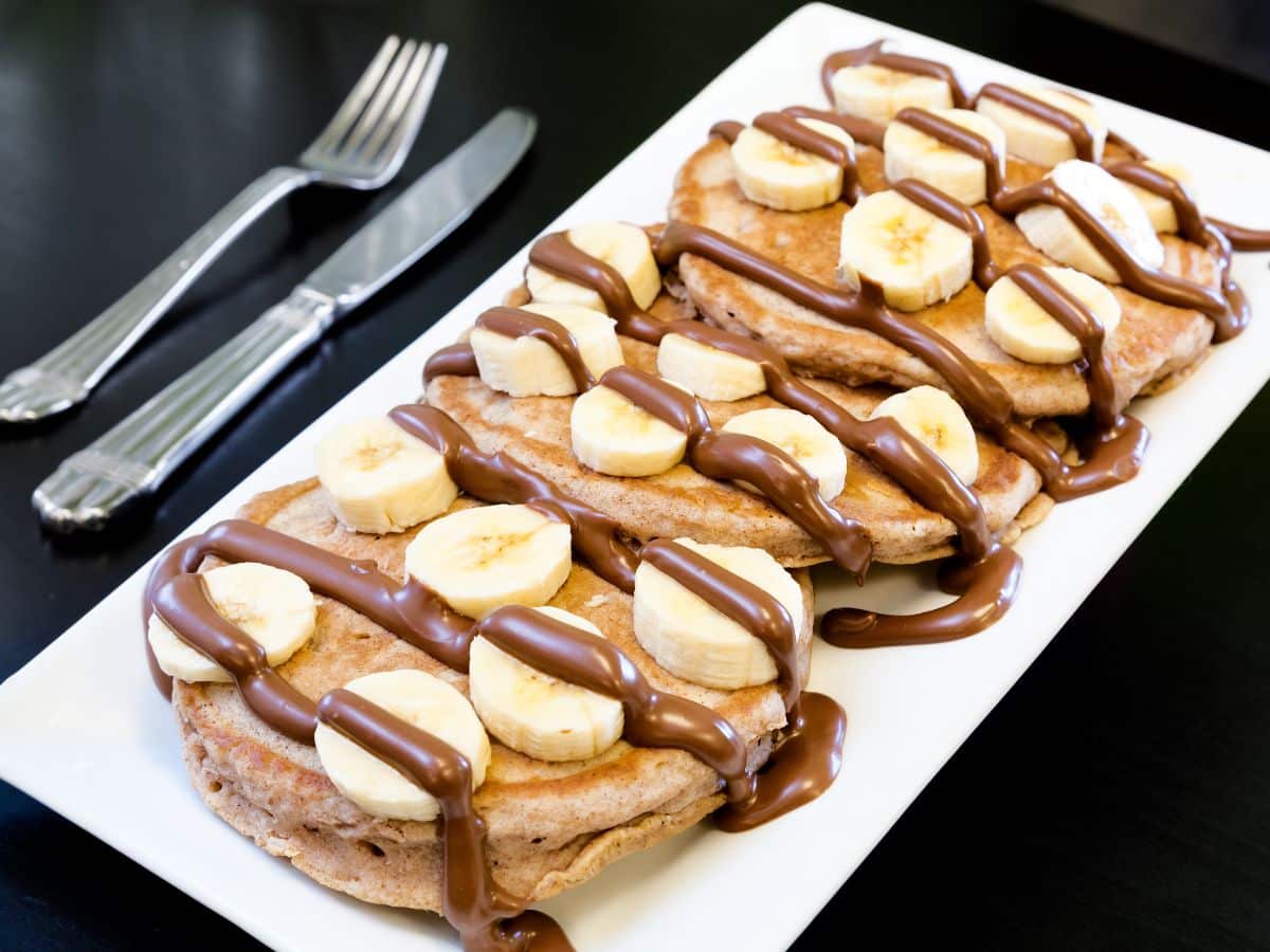 A plate of vegan pancakes with dairy-free Nutella and bananas.