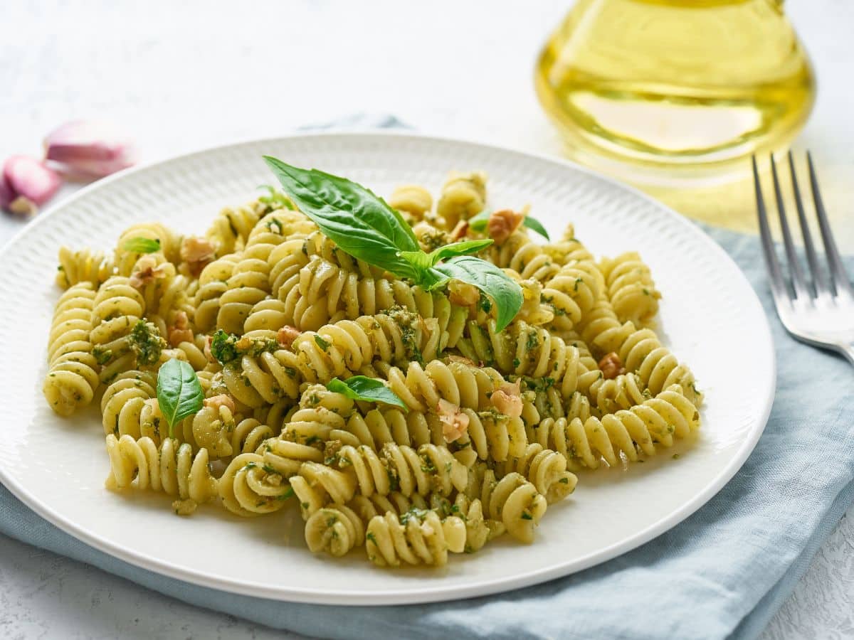 Pesto pasta on a white plate with garlic and basil.