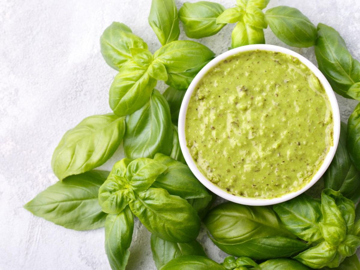 A bowl of pesto sauce surrounded by basil leaves.