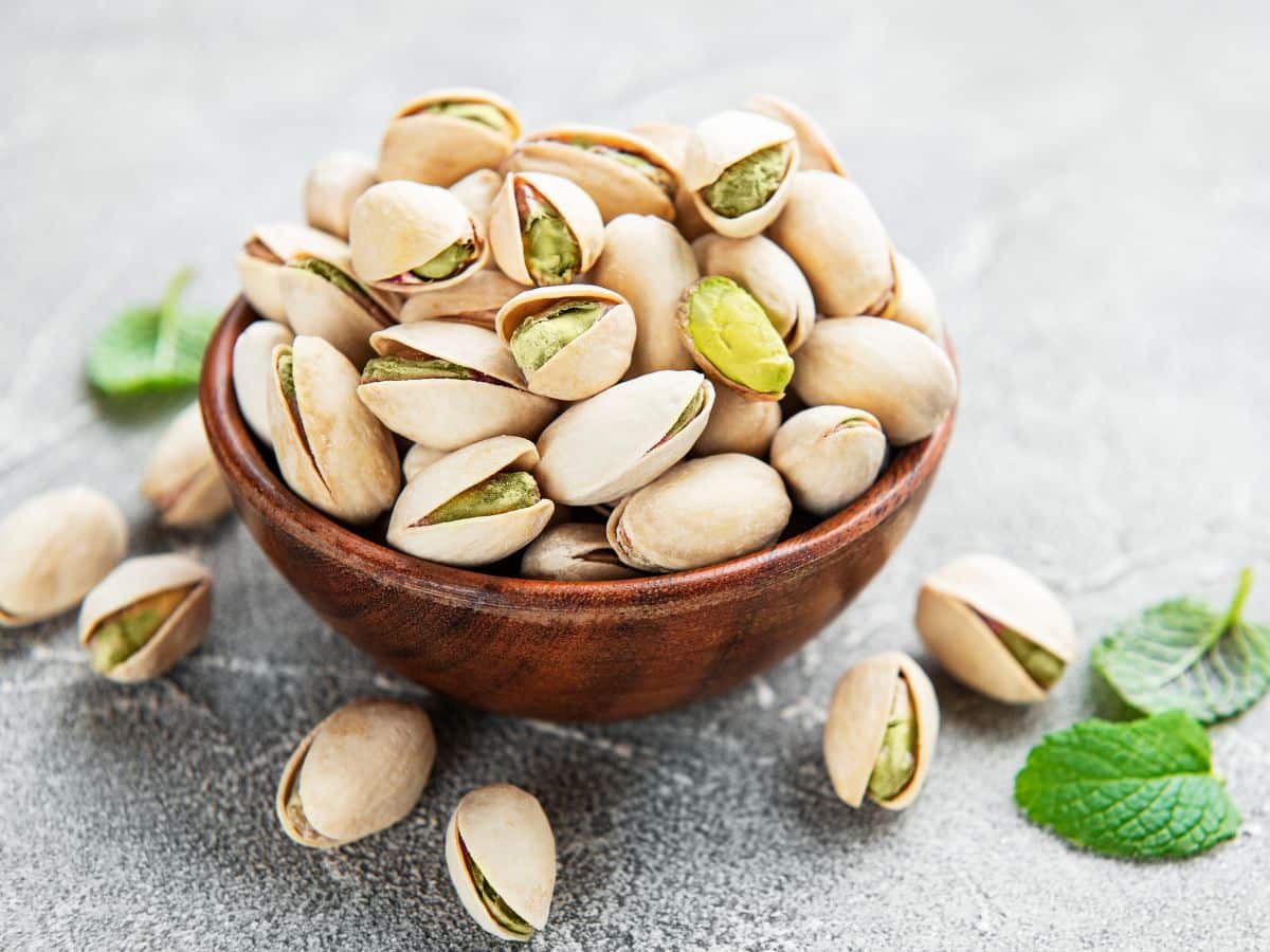 Unshelled pistachios in a wooden bowl accented with mint leaves.