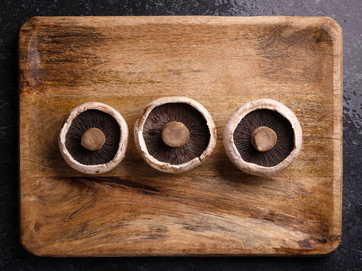 Three portobello mushrooms on a wooden cutting board.