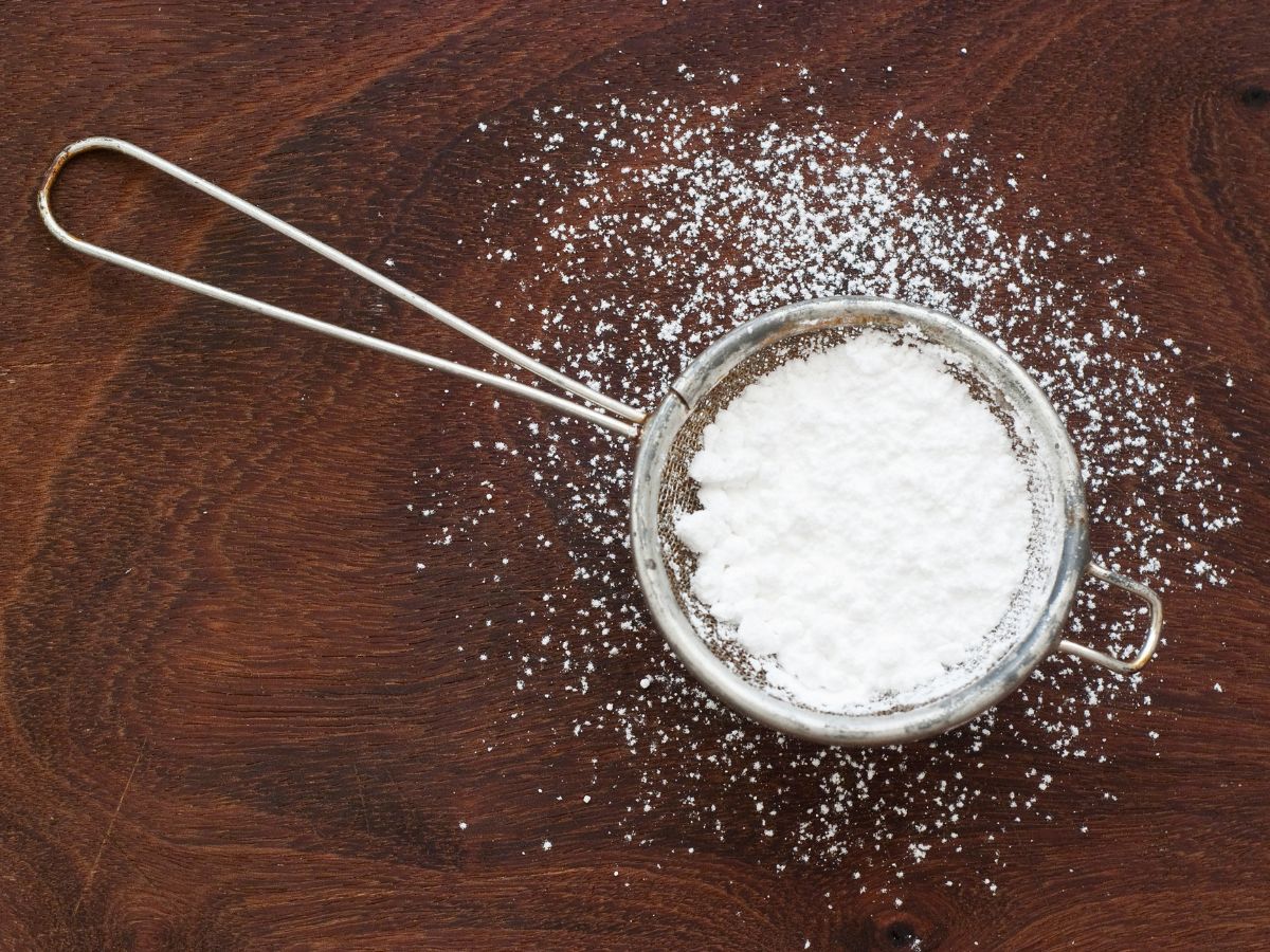 A sifter full of powdered sugar sitting on a dark wood table.