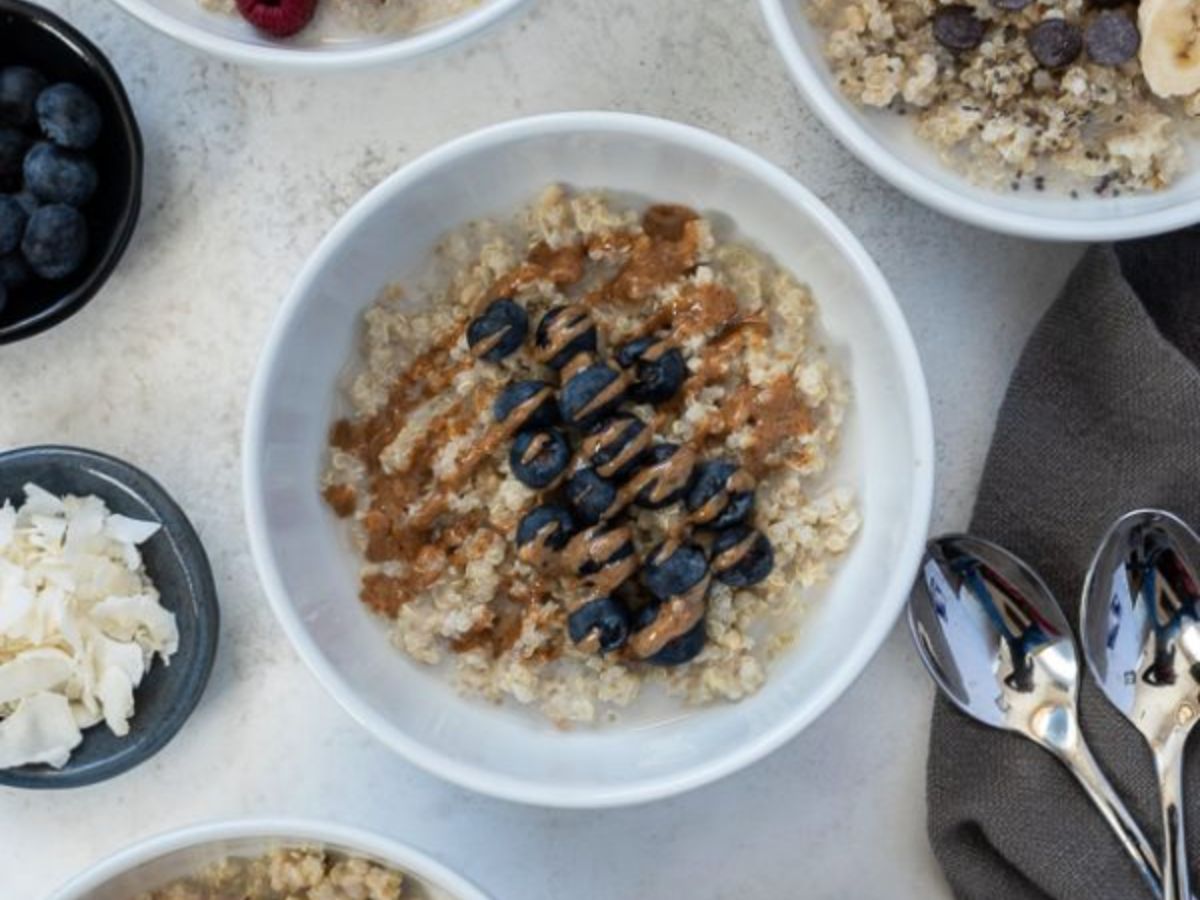 Four bowls of quinoa oatmeal with toppings and spoons.
