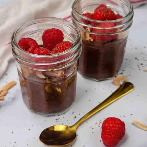 Jars of chocolate chia seed pudding topped with raspberries.