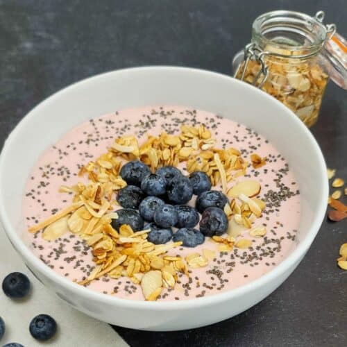 A bowl of strawberry Greek yogurt topped with blueberries, chia seeds, and granola.