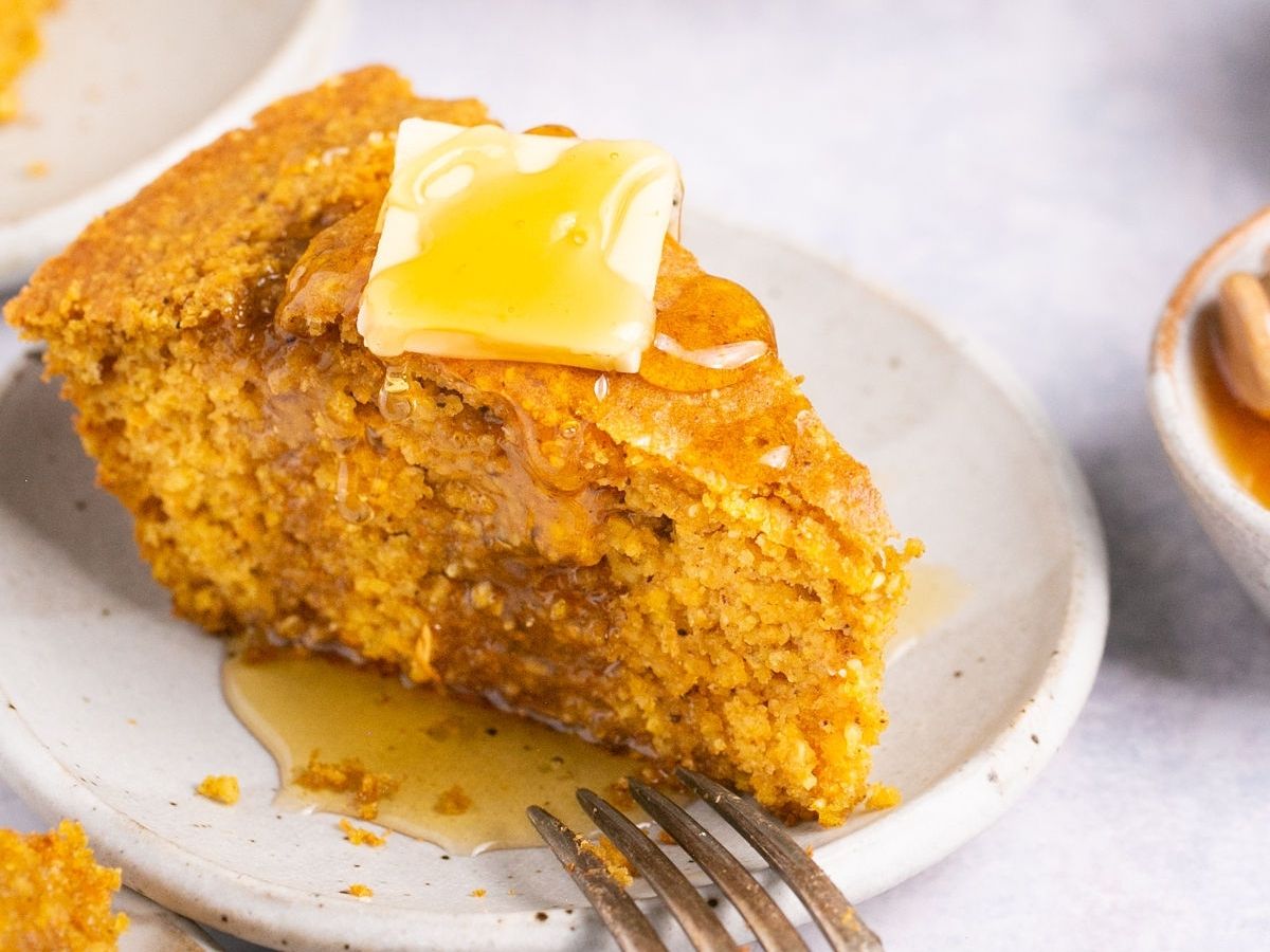 A slice of sweet potato cornbread topped with a pat of butter and a drizzle of pure maple syrup.