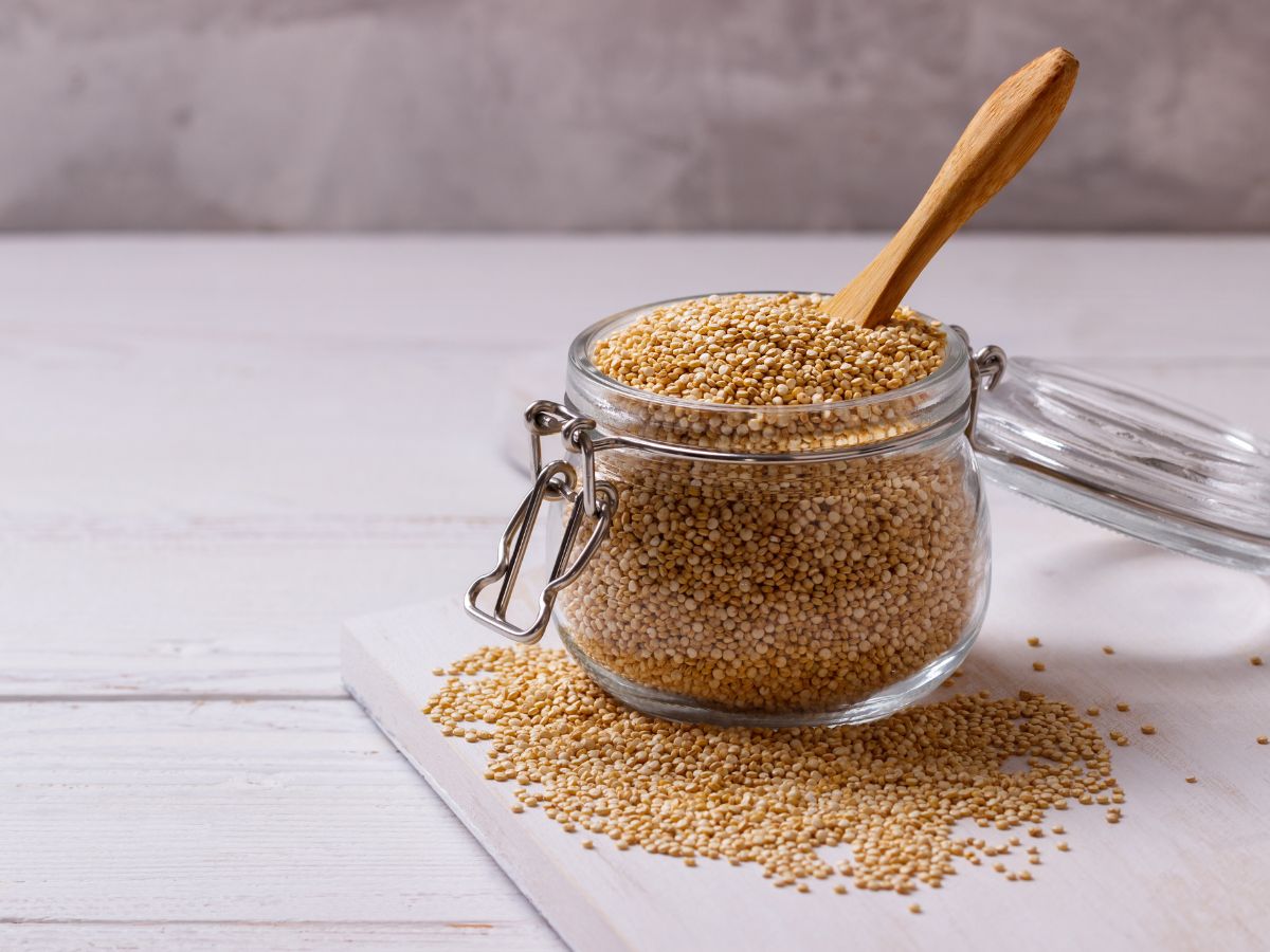 Uncooked quinoa in a glass jar with a wooden spoon.