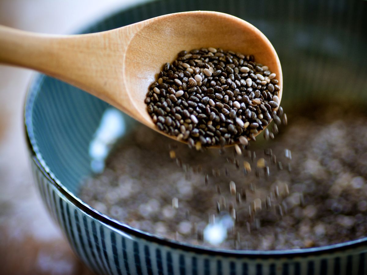 A wooden spoon is pouring nutritious chia seeds into a bowl, highlighting their benefits.