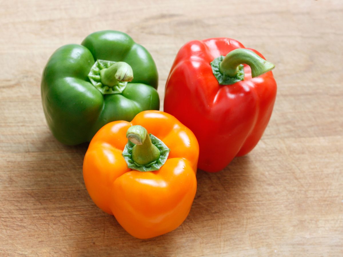 Three different colored bell peppers on a wooden table.