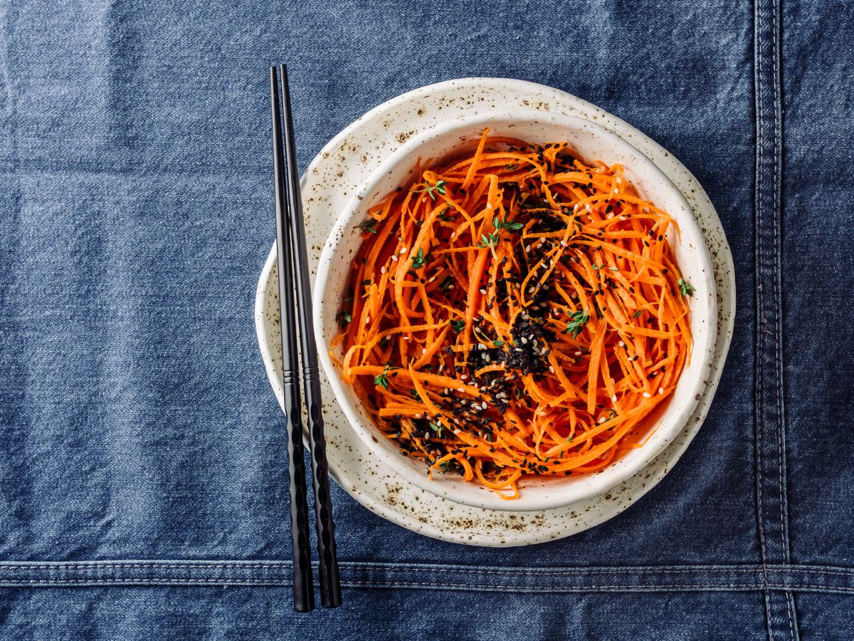 A bowl of carrot noodles with chopsticks on a blue cloth.
