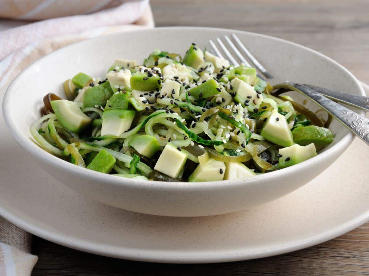 A bowl of cucumber noodle salad with a fork.