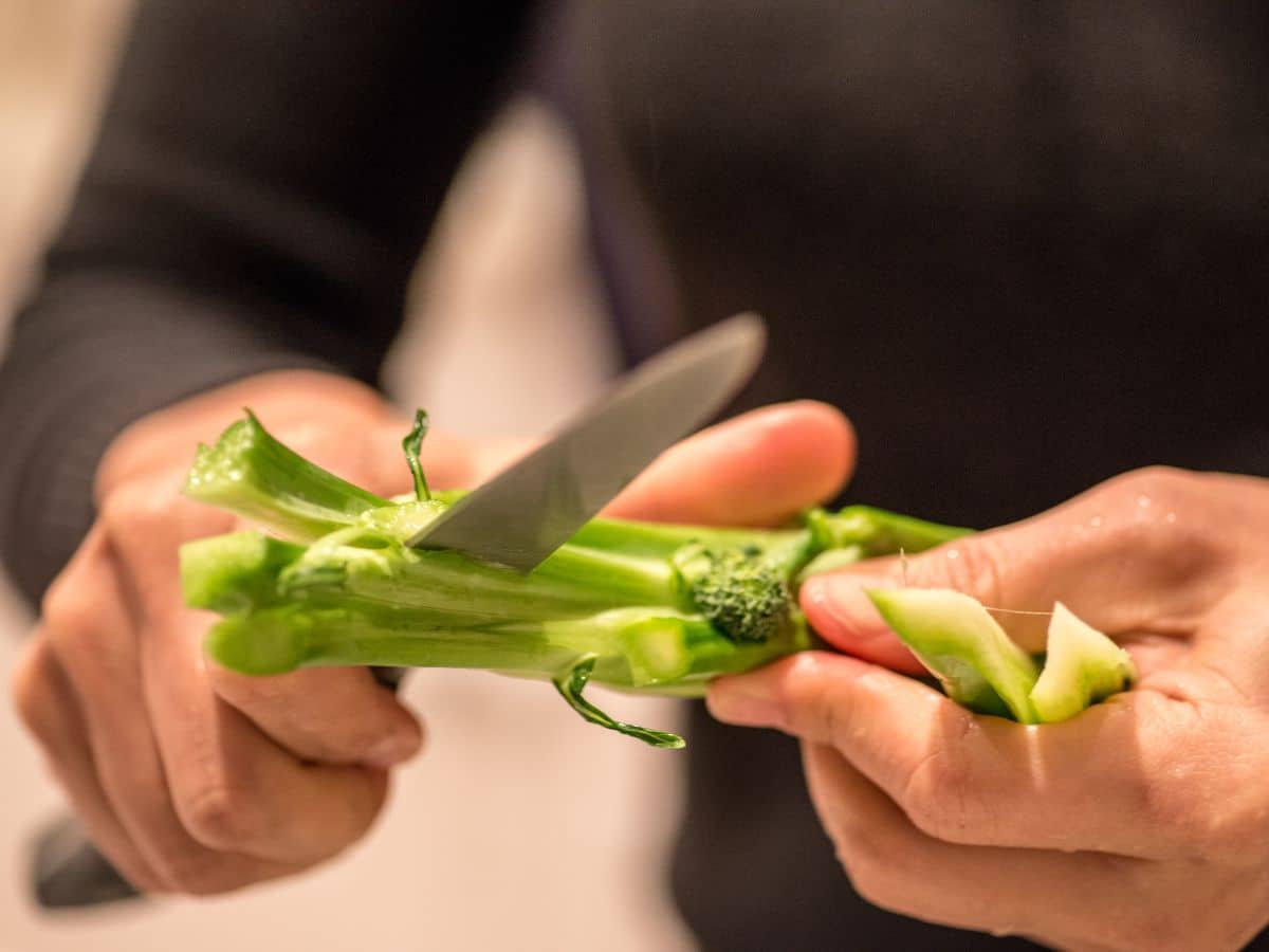 A person cutting broccoli stalks with a knife.