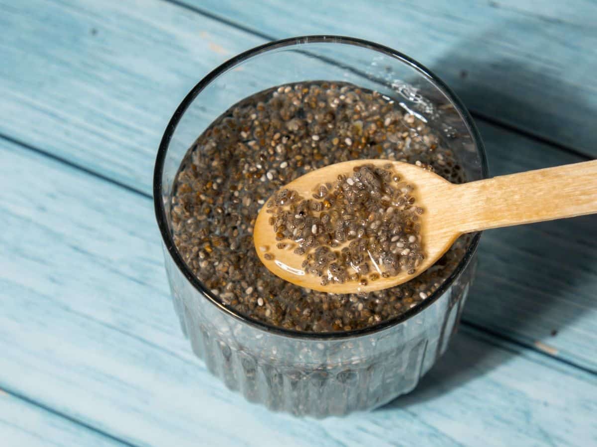 Soaked chia seeds on a wooden spoon above a glass.