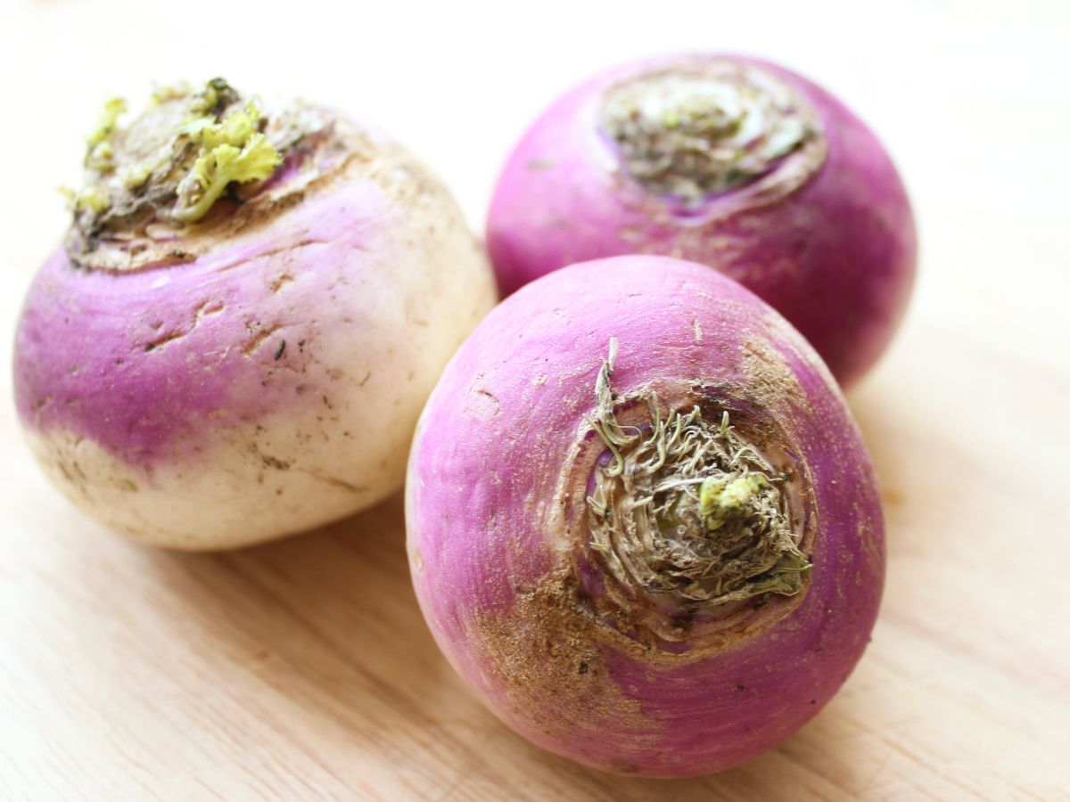 Three purple and white turnips on a wooden table.