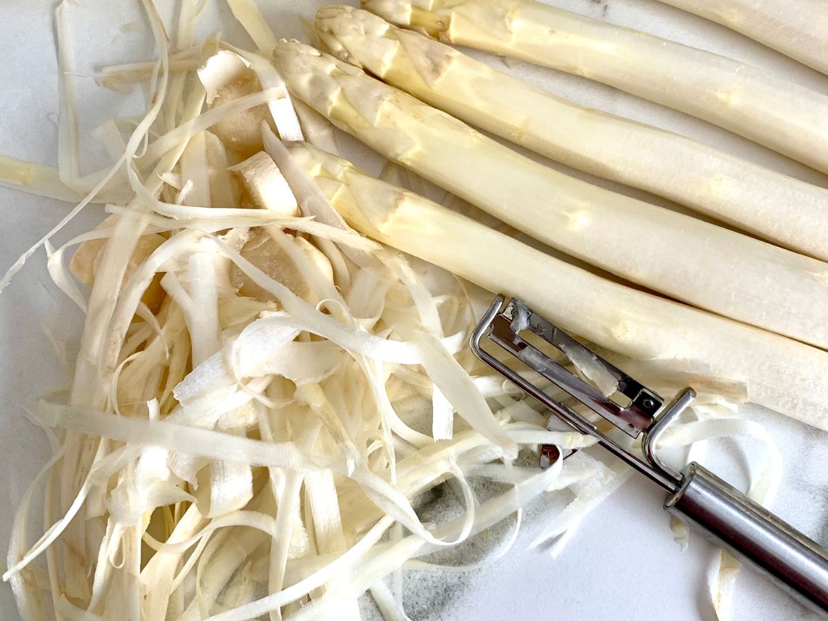 A vegetable peeler being used to cut white asparagus into vegetable noodles.