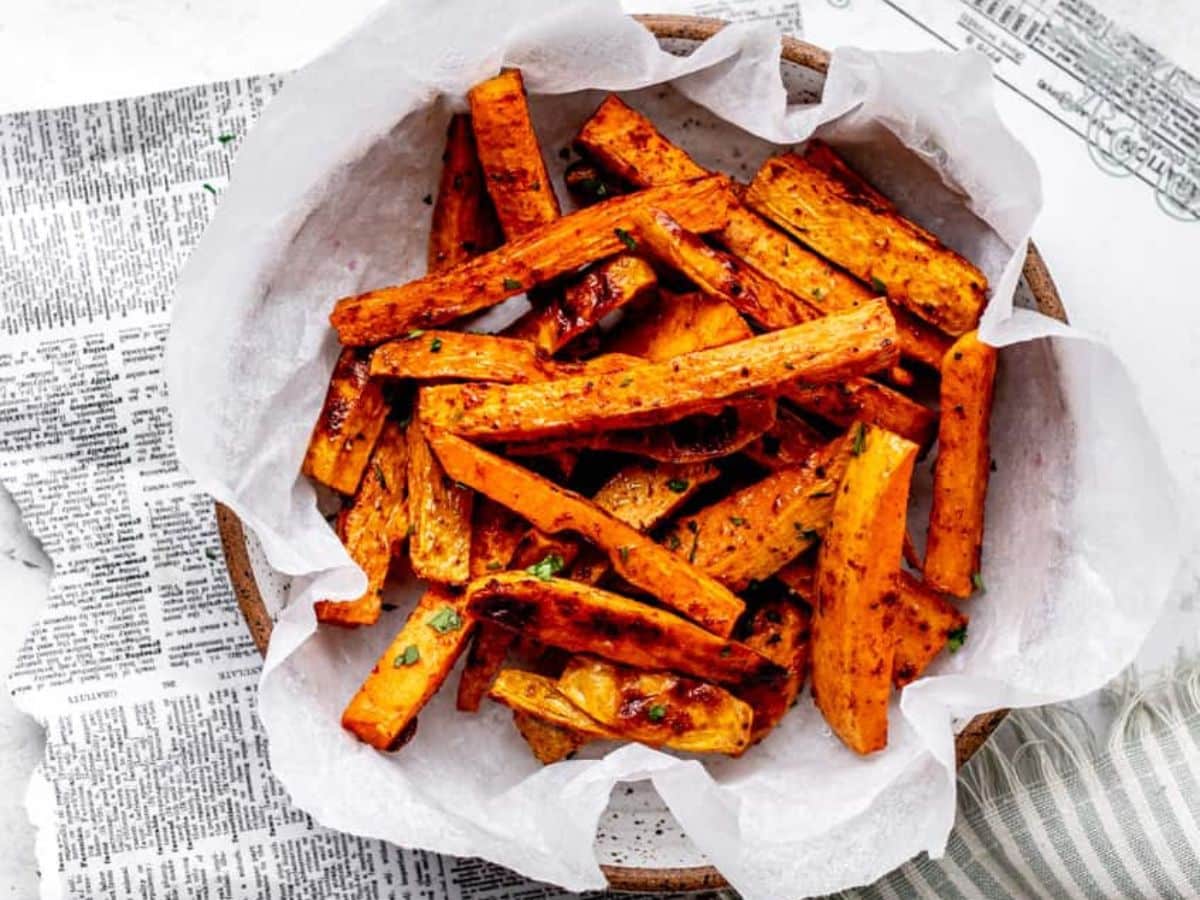 Roasted sweet potato fries in a bowl on a newspaper.
