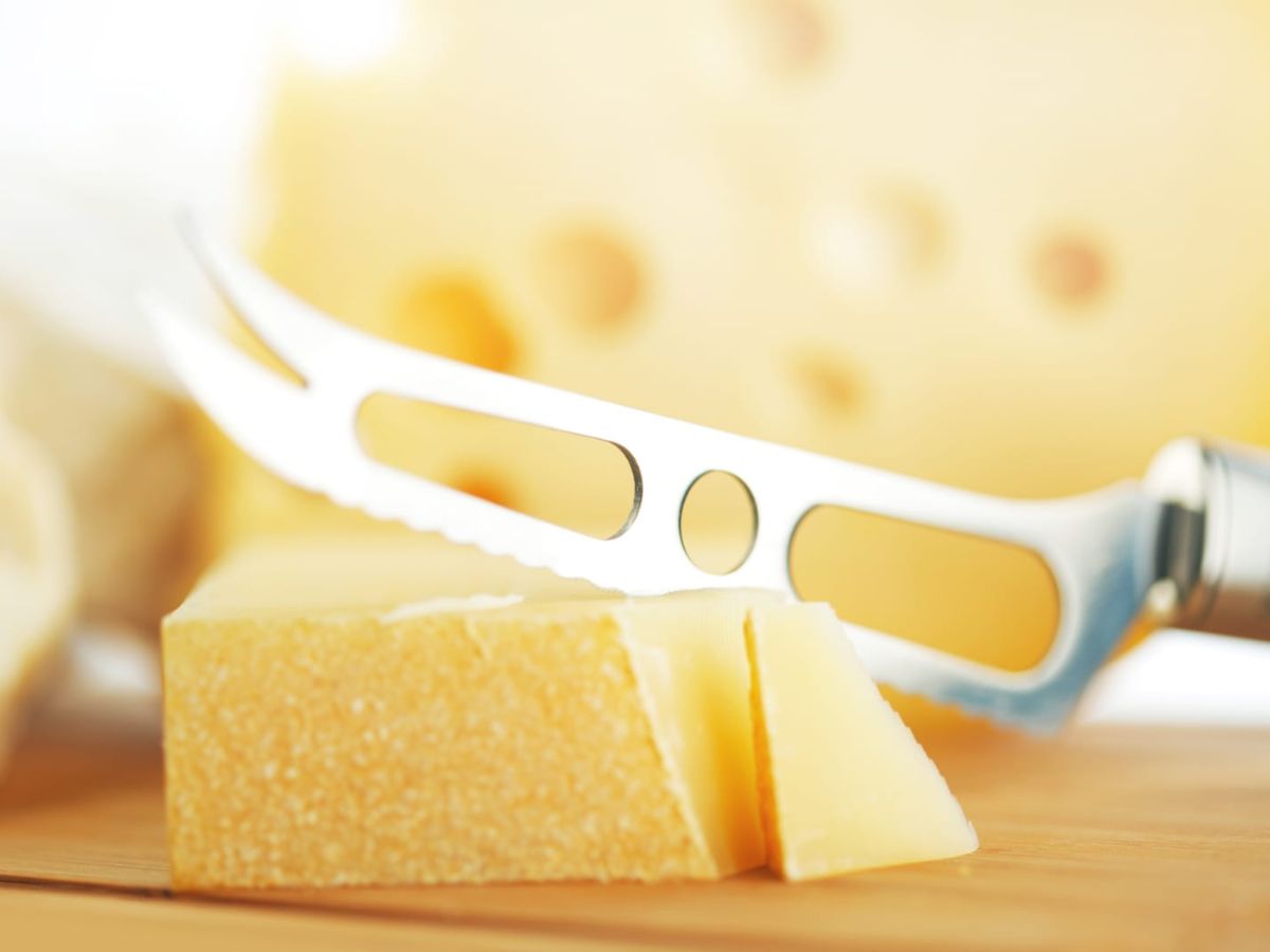 A cheese knife cutting into a hard cheese.