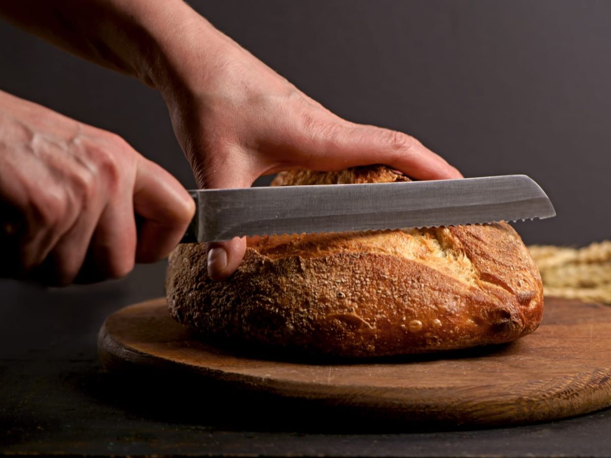 A person cutting a loaf of bread on a wooden board.