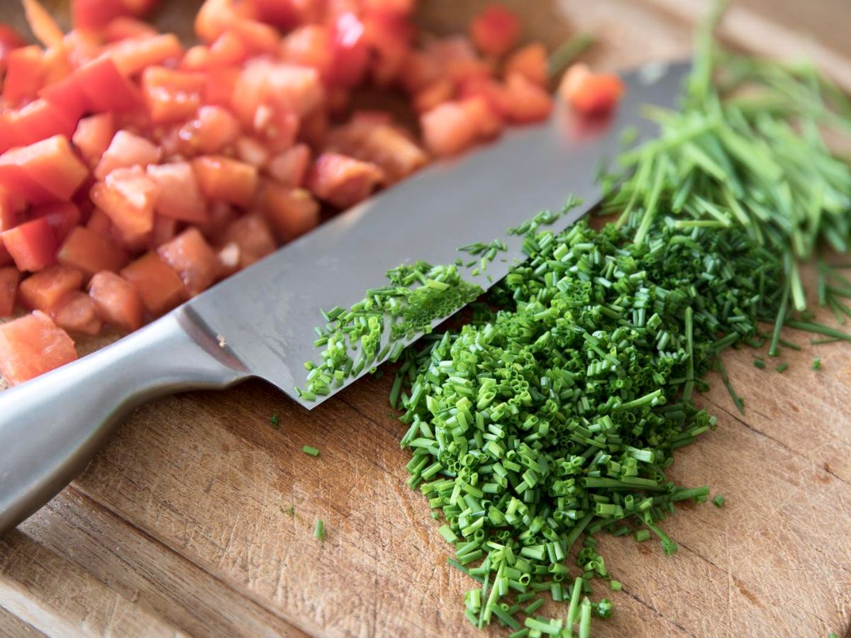 A knife on a cutting board with tomatoes and chives.