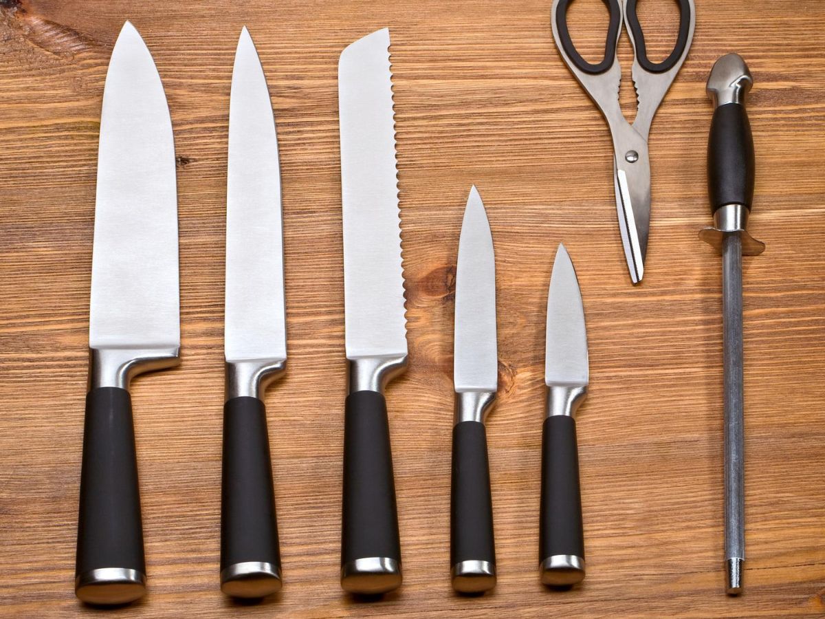A group of chef's knives and scissors on a wooden table.