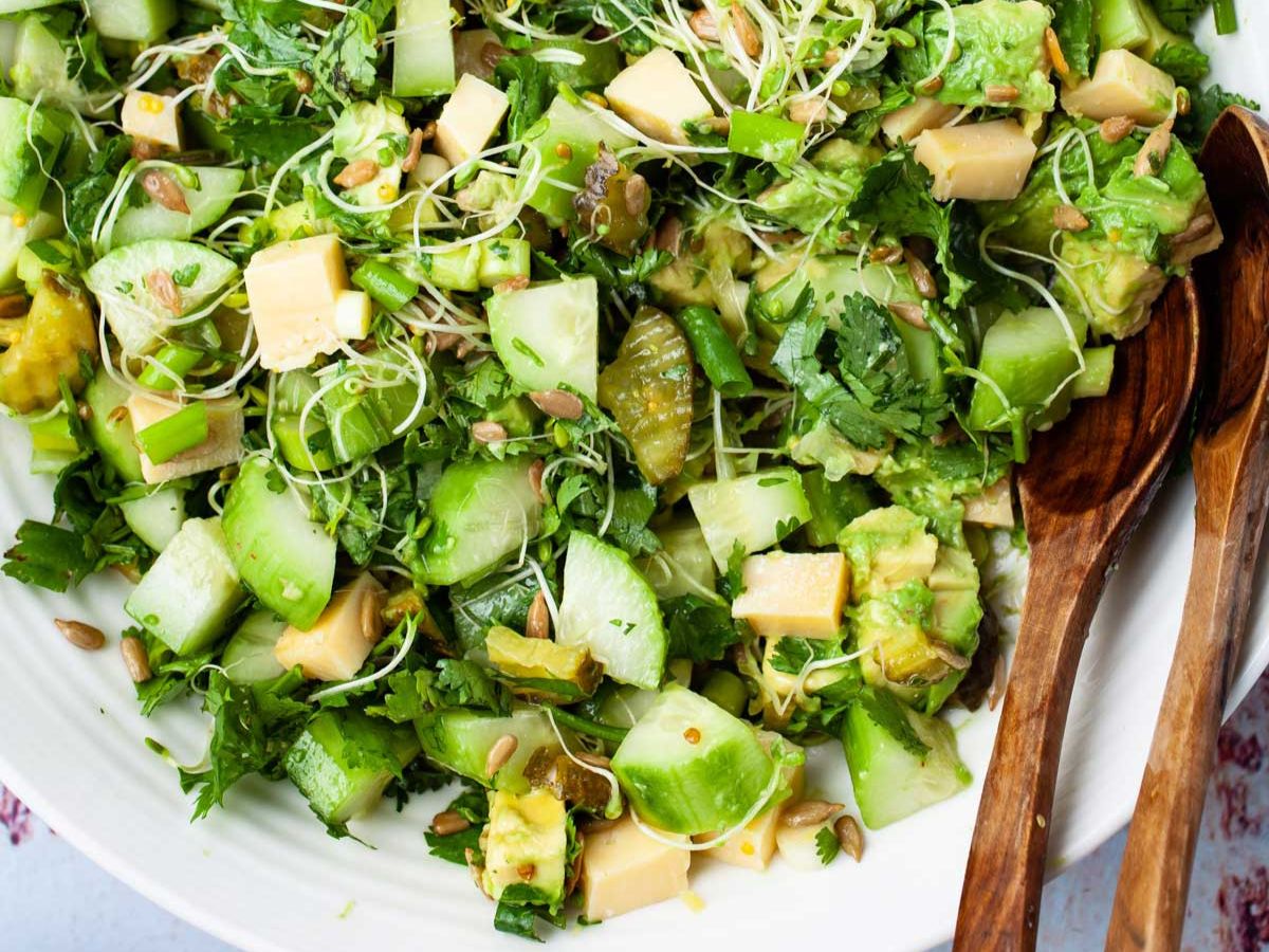 A bowl of green salad with a wooden spoon.