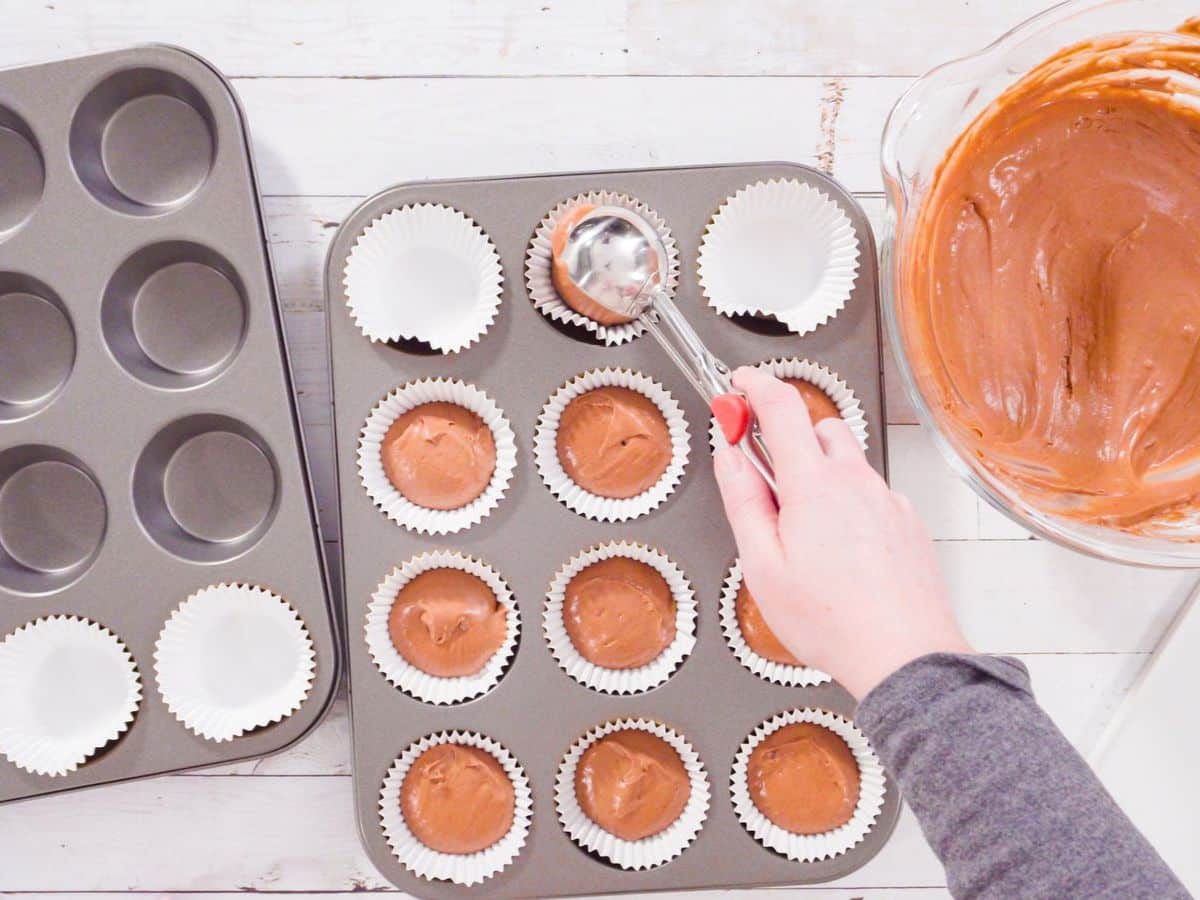 A person pouring chocolate into cupcakes in a muffin tin.