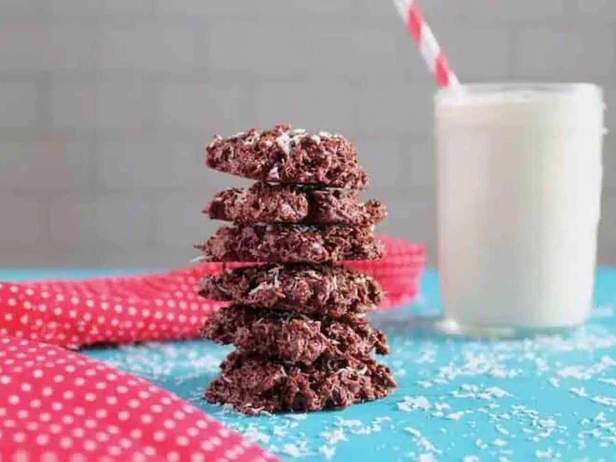 A stack of chocolate coconut cookies next to a glass of milk.